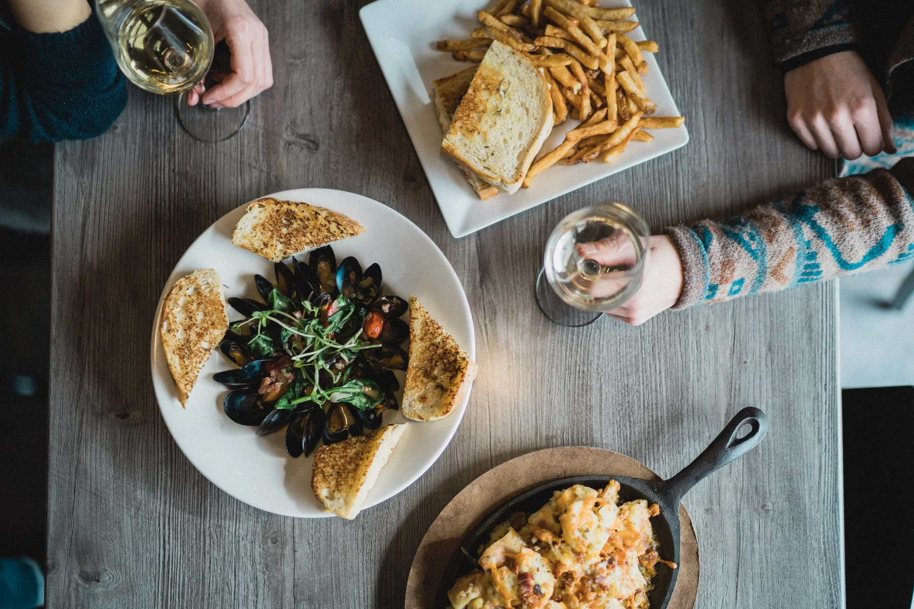 An overhead view of food, drinks and hands around a restaurant table